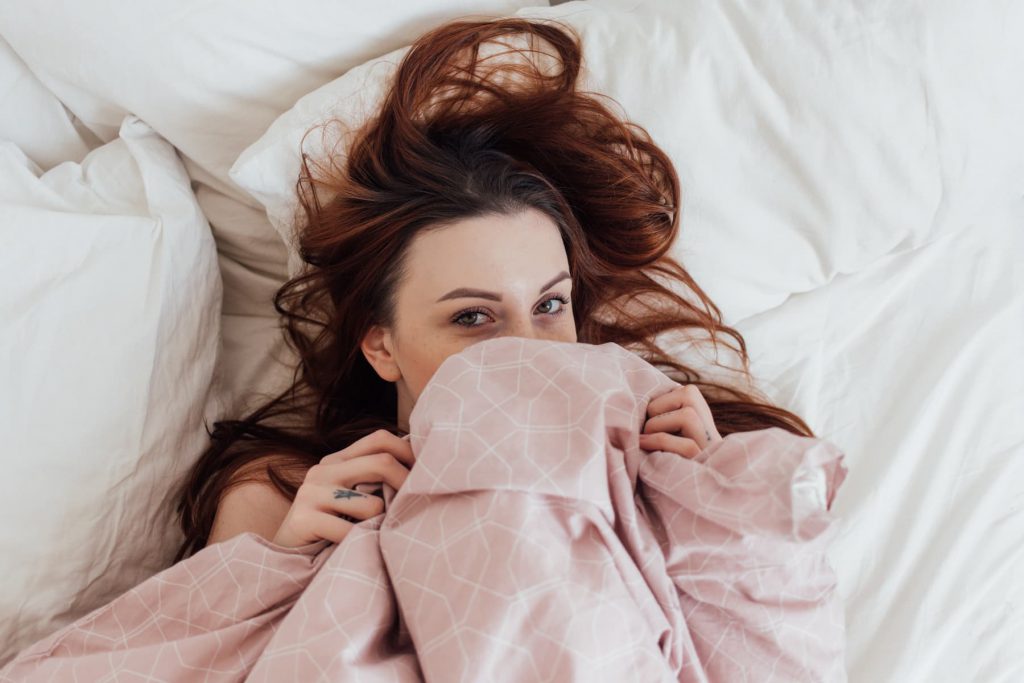 Young redhead woman under bed sheets.